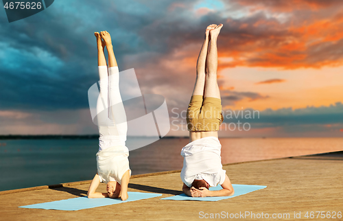 Image of couple making yoga headstand on mat outdoors