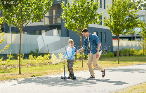 Image of happy father and little son riding scooter in city