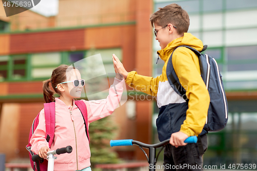 Image of happy school children with backpacks and scooters