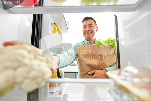 Image of man putting new purchased food to home fridge