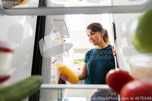 Image of happy woman taking juice from fridge at home