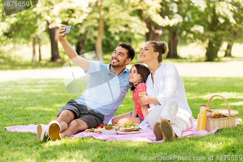 Image of family having picnic and taking selfie at park