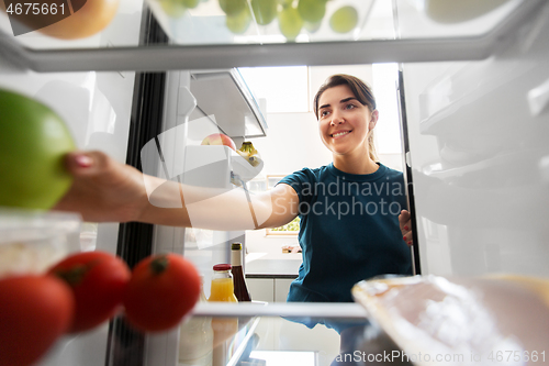 Image of happy woman taking food from fridge at home