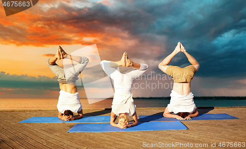 Image of people making yoga headstand on mat outdoors