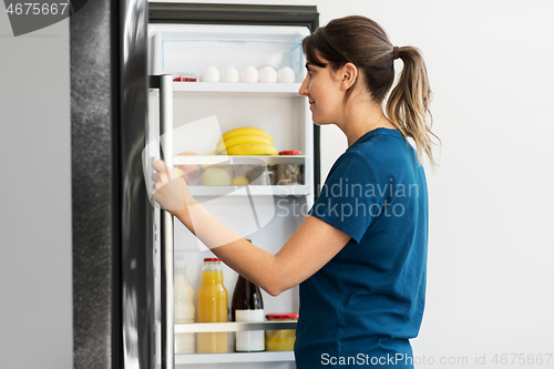 Image of happy woman at open fridge at home kitchen