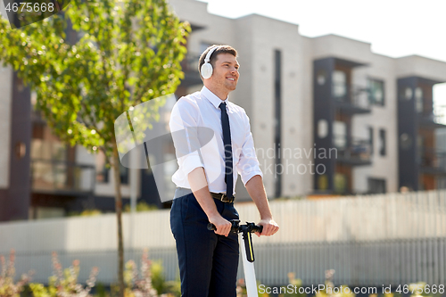 Image of businessman with headphones riding scooter in city