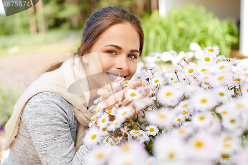 Image of happy woman smelling chamomile flowers in garden