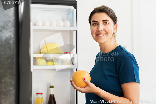 Image of happy woman taking food from fridge at home