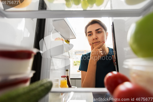 Image of thoughtful woman at open fridge at home kitchen