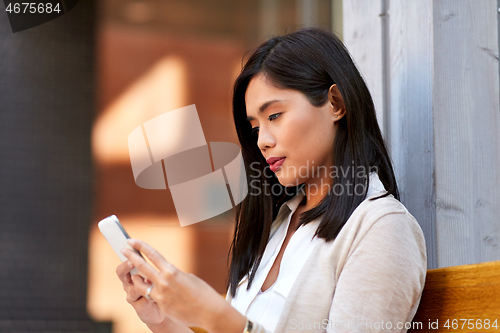 Image of asian woman using smartphone sitting on bench