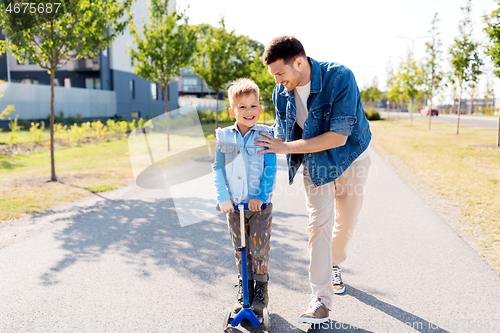 Image of happy father and little son riding scooter in city