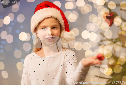 Image of happy girl in santa hat decorating christmas tree