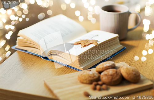 Image of book with autumn leaf, cookies and tea on table