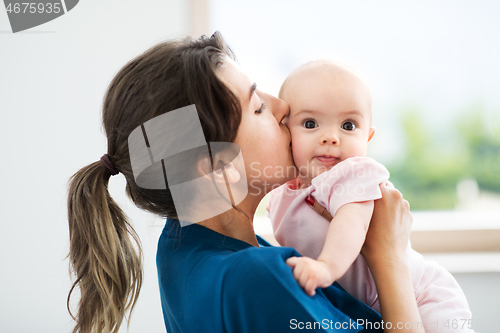 Image of mother holding and kissing baby daughter at home