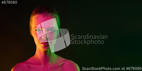 Image of Portrait of female fashion model in neon light on dark studio background.