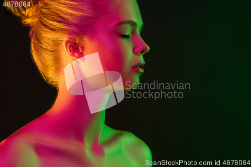 Image of Portrait of female fashion model in neon light on dark studio background.