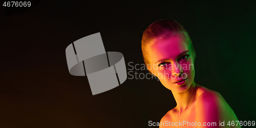 Image of Portrait of female fashion model in neon light on dark studio background.