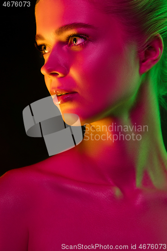 Image of Portrait of female fashion model in neon light on dark studio background.