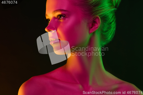 Image of Portrait of female fashion model in neon light on dark studio background.