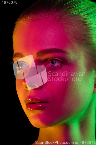 Image of Portrait of female fashion model in neon light on dark studio background.