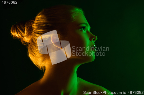 Image of Portrait of female fashion model in neon light on dark studio background.