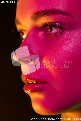 Image of Portrait of female fashion model in neon light on dark studio background.