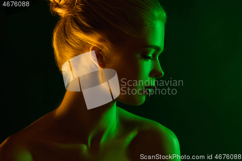 Image of Portrait of female fashion model in neon light on dark studio background.