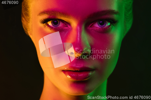 Image of Portrait of female fashion model in neon light on dark studio background.