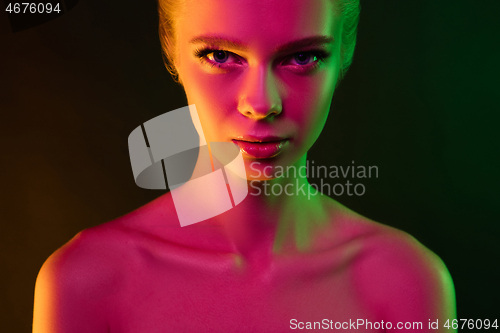 Image of Portrait of female fashion model in neon light on dark studio background.