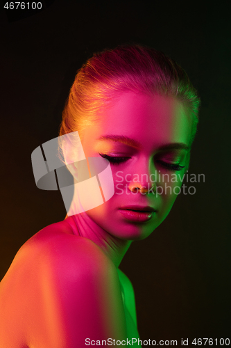 Image of Portrait of female fashion model in neon light on dark studio background.