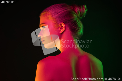 Image of Portrait of female fashion model in neon light on dark studio background.