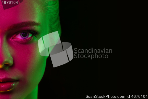 Image of Portrait of female fashion model in neon light on dark studio background.