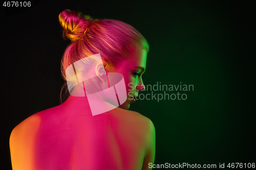 Image of Portrait of female fashion model in neon light on dark studio background.