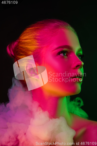 Image of Portrait of female fashion model in neon light on dark studio background.