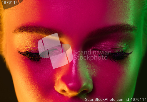 Image of Close up portrait of female fashion model in neon light on dark studio background.