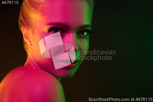 Image of Portrait of female fashion model in neon light on dark studio background.