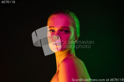 Image of Portrait of female fashion model in neon light on dark studio background.