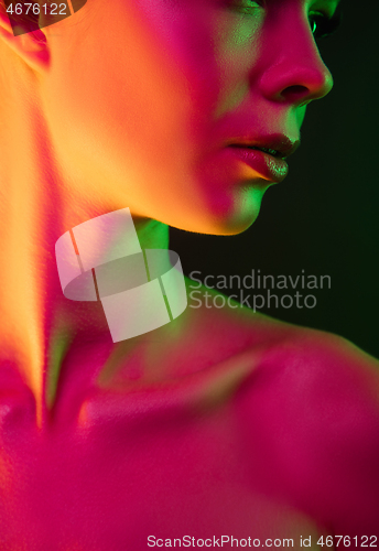 Image of Portrait of female fashion model in neon light on dark studio background.