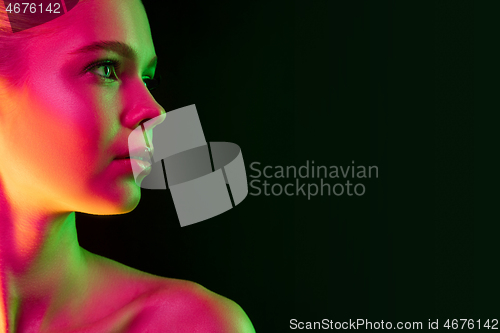 Image of Portrait of female fashion model in neon light on dark studio background.