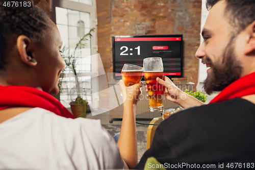 Image of TV screen with mobile app for betting and score, cheering friends, fans in front of it look excited
