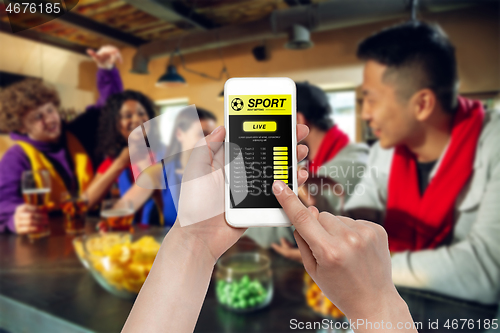 Image of Device screen with mobile app for betting and score, cheering friends, fans on background