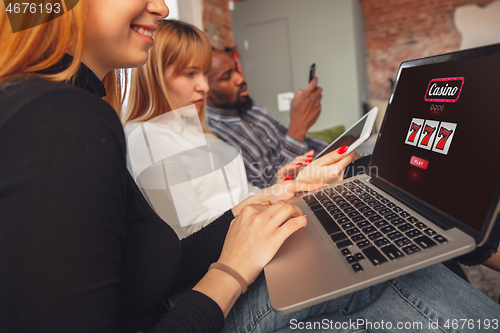 Image of Friends using laptop with mobile app for online casino, cheering people look excited