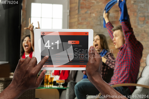 Image of Device screen with mobile app for betting and score, cheering friends, fans on background