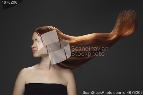 Image of Beautiful model with long smooth, flying red hair isolated on dark studio background.