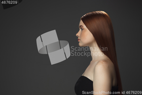 Image of Beautiful model with long smooth, flying red hair isolated on dark studio background.