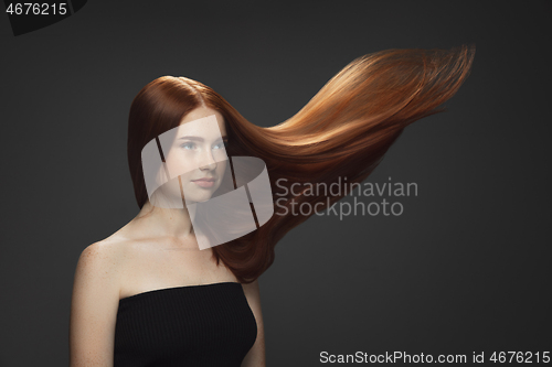 Image of Beautiful model with long smooth, flying red hair isolated on dark studio background.