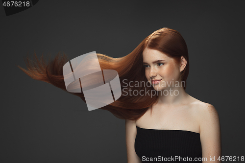 Image of Beautiful model with long smooth, flying red hair isolated on dark studio background.