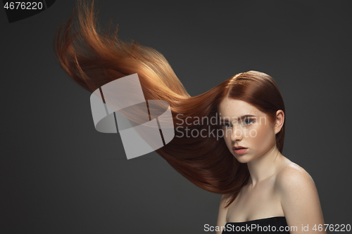 Image of Beautiful model with long smooth, flying red hair isolated on dark studio background.