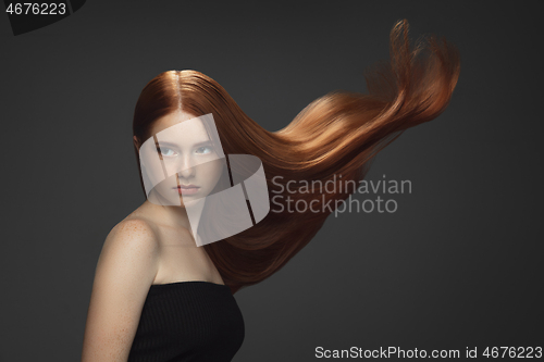 Image of Beautiful model with long smooth, flying red hair isolated on dark studio background.