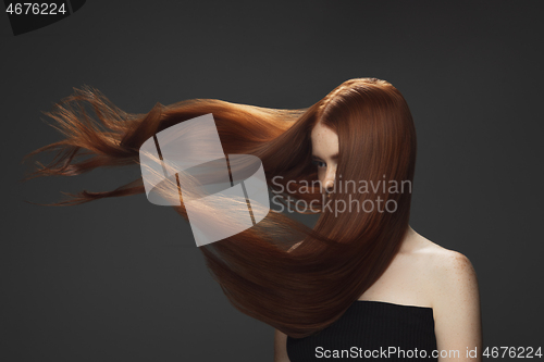 Image of Beautiful model with long smooth, flying red hair isolated on dark studio background.